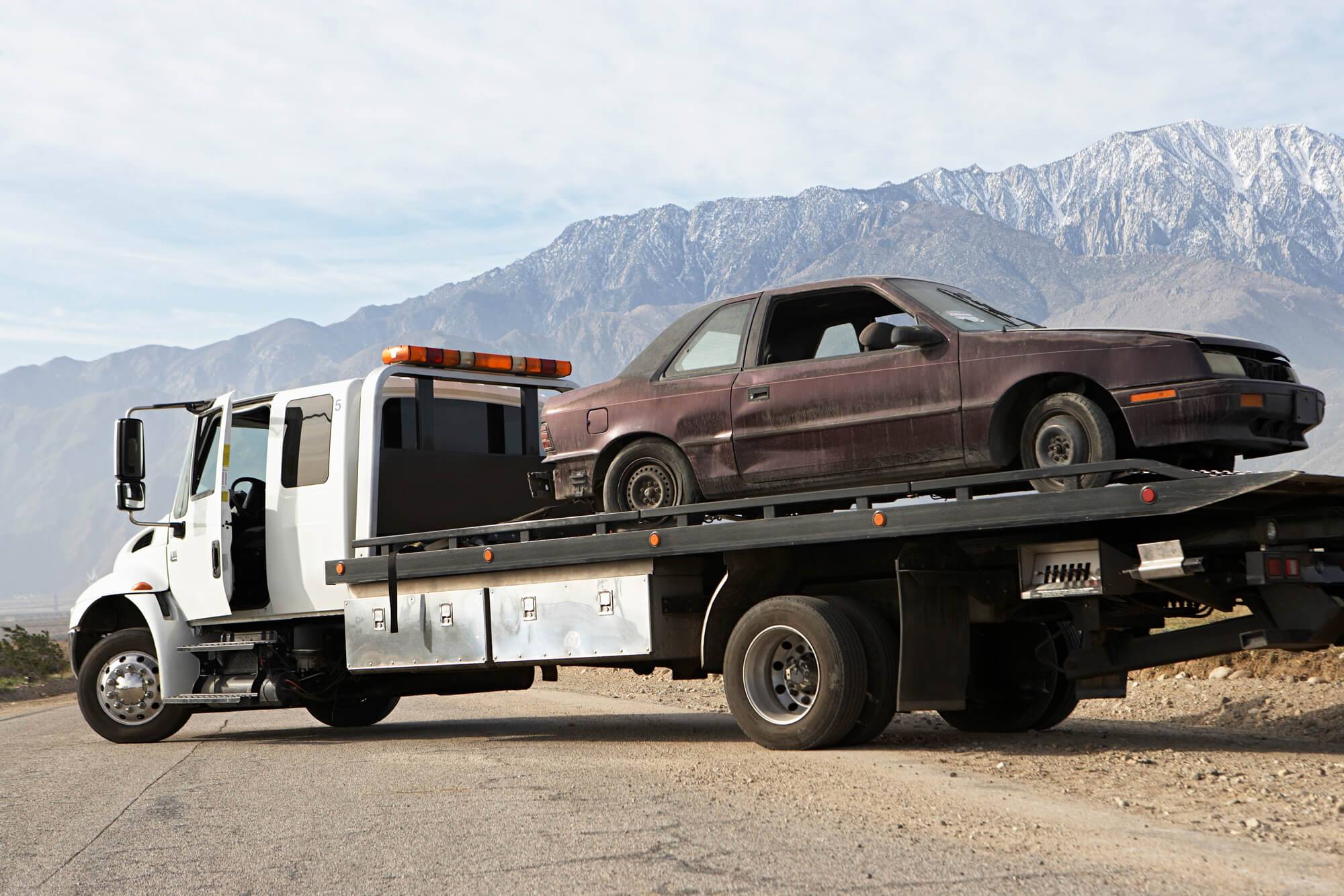 Junk Car Towtruck Flatbed Across Road Mountains
